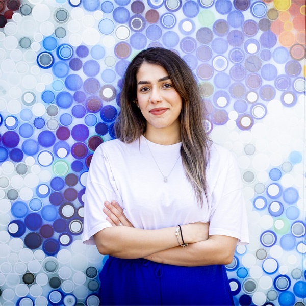 A female student with long hair and wearing a white tshirt is standing confidently smiling for a photo