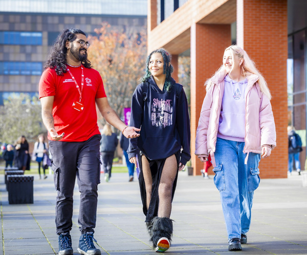 A male student ambassador wearing red uniform is showing two female visitors around campus