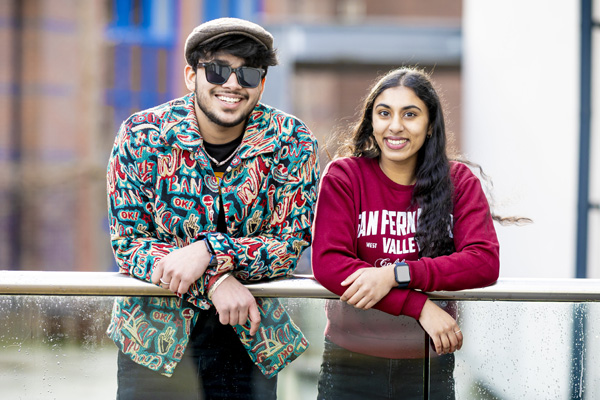A male student and a female student are smiling, posing casually outside on campus for a photography
