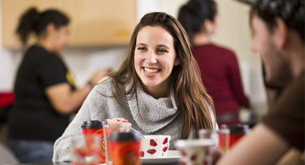 A female with brown hair wearing a grey jumper is sitting at the dining table socialising