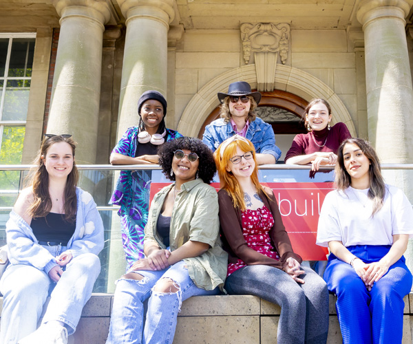 A group of casually dressed students are smiling outside the library
