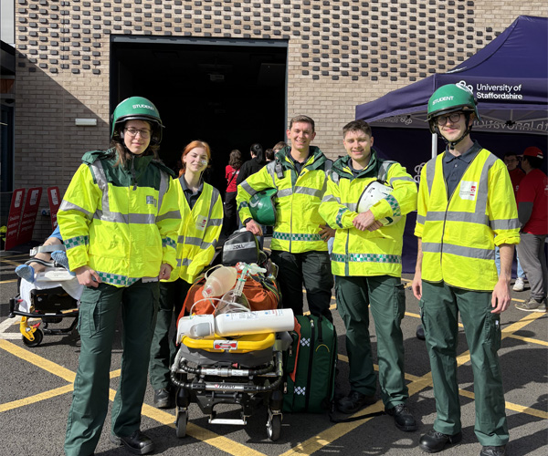 Students wearing paramedic uniforms are standing with medical equipment for a photo