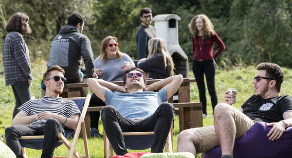 A group of casually dressed students are relaxing and socialised outside in green space