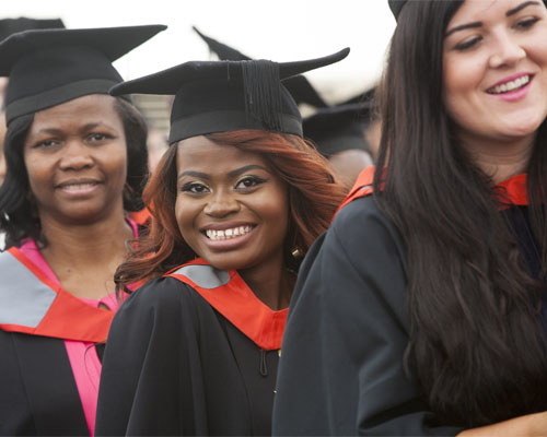 Female graduates wearing black caps and gowns are smiling at a graduation event