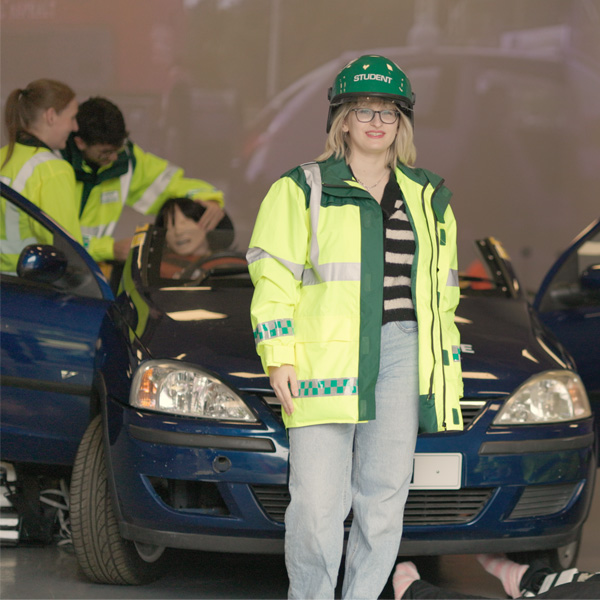 Students wearing paramedic uniforms are taking part in a live simulation involving a car and dummy patient