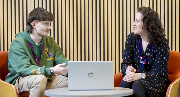 A male student is sat down chatting with a female advisor in a modern breakout area