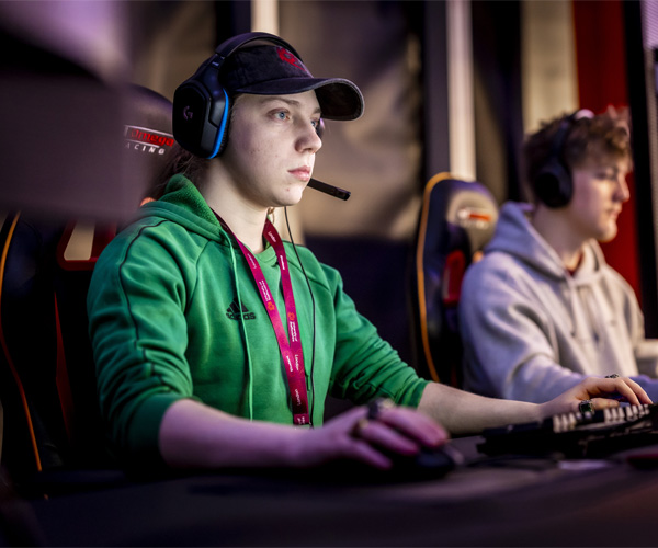 A male student wearing a cap and headset is using the gaming computers